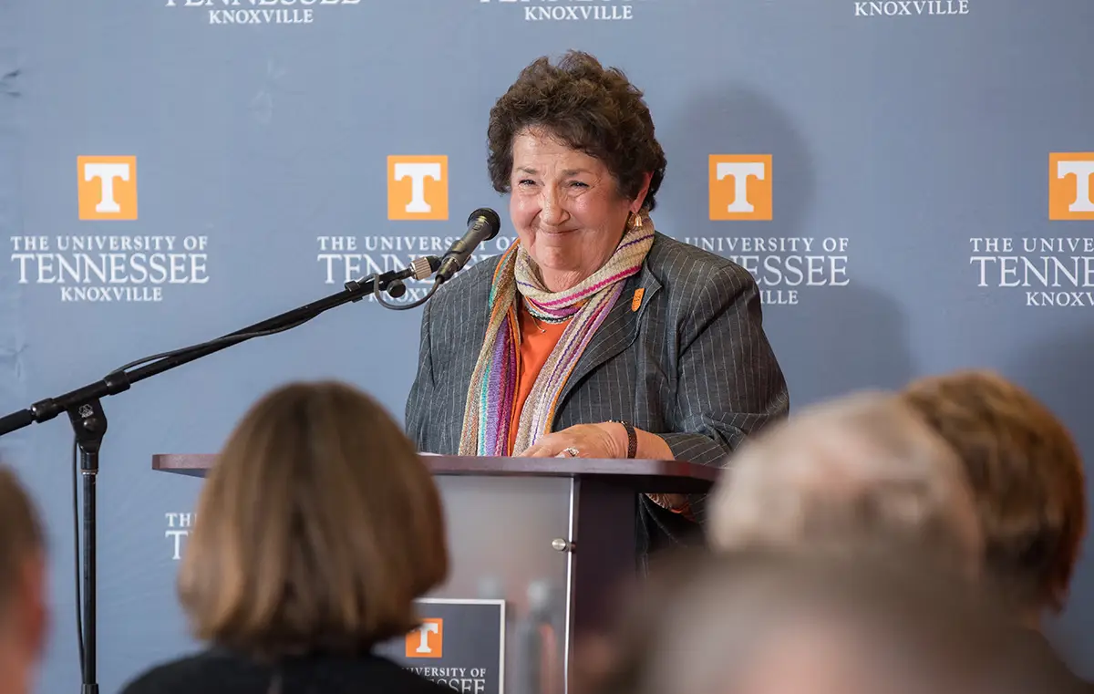 A woman speaking at a podium with the UT logo behind her