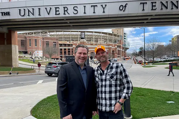 Roger Clark and Rob Wiethoff posing for a photo in front of the UT Pedestrian Bridge