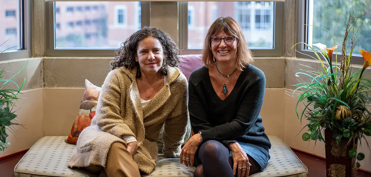 AJRC co-directors Wendy Bach and Michelle Brown pose for a photo while seated in front of a window