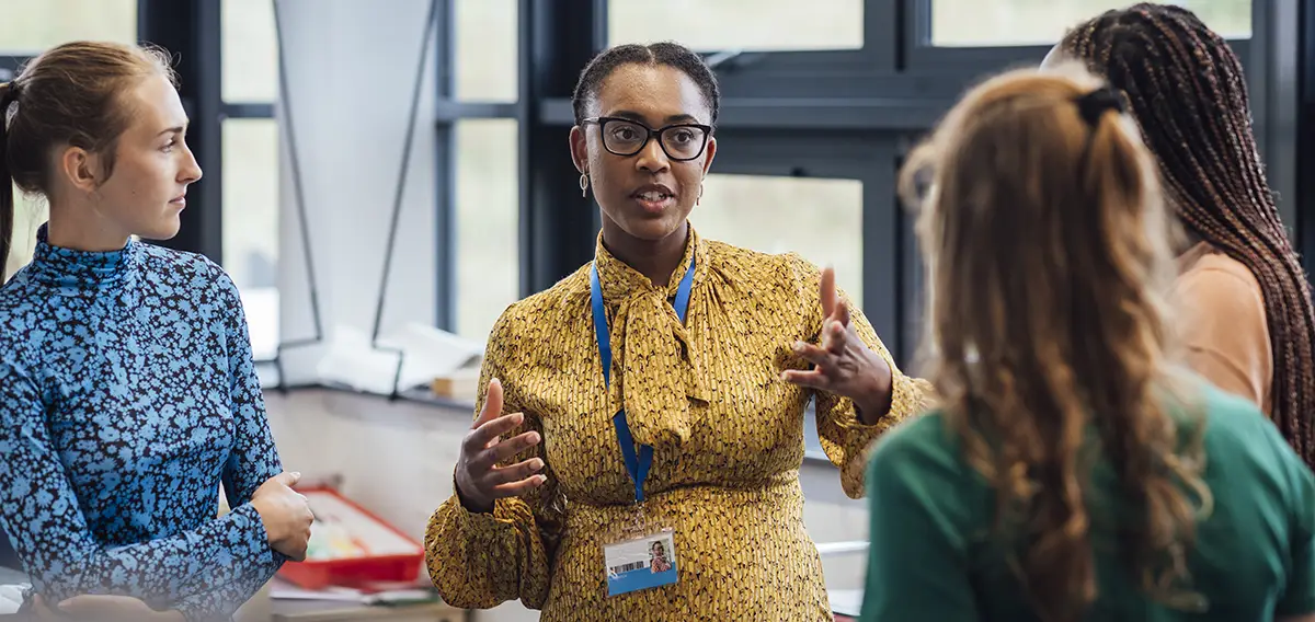 A Black woman leads a discussion with other women in a large, open space