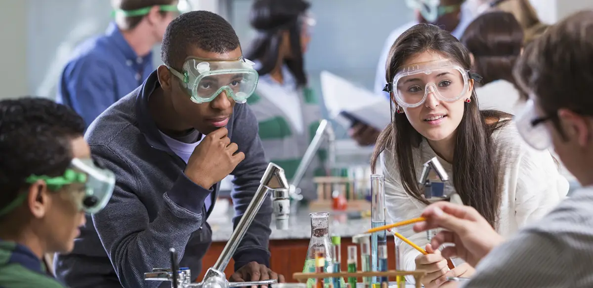 Students collaborate in a chemistry lab while wearing safety goggles