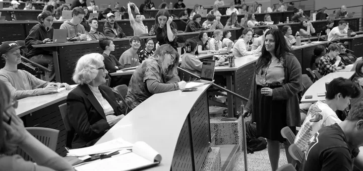 A black and white photo of Maggie Mamantov teaching a large lecture class with Charmaine Mamantov in the audience