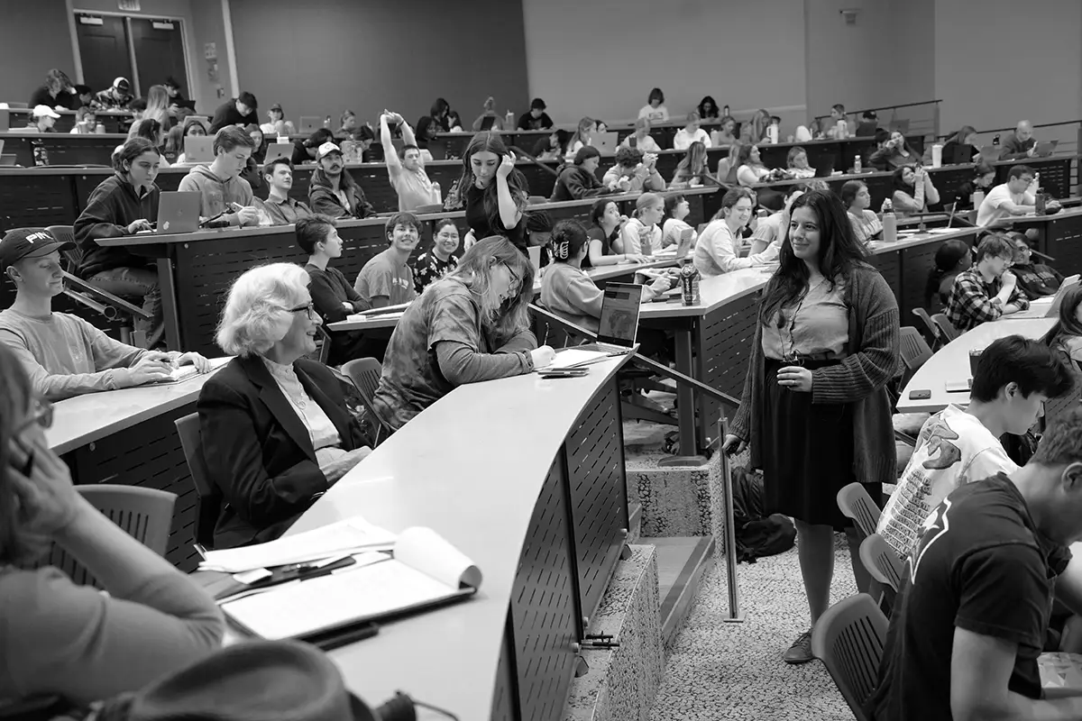 A black and white photo of Maggie Mamantov teaching a large lecture class with Charmaine Mamantov in the audience