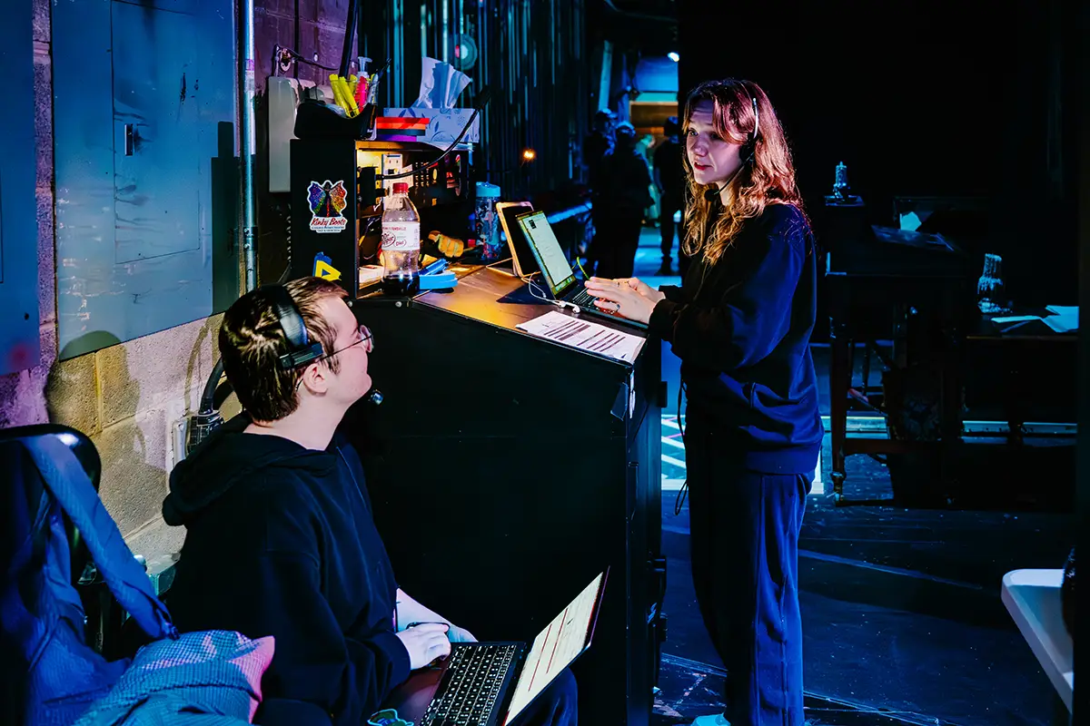 Two crew members talking behind the scenes while using laptops